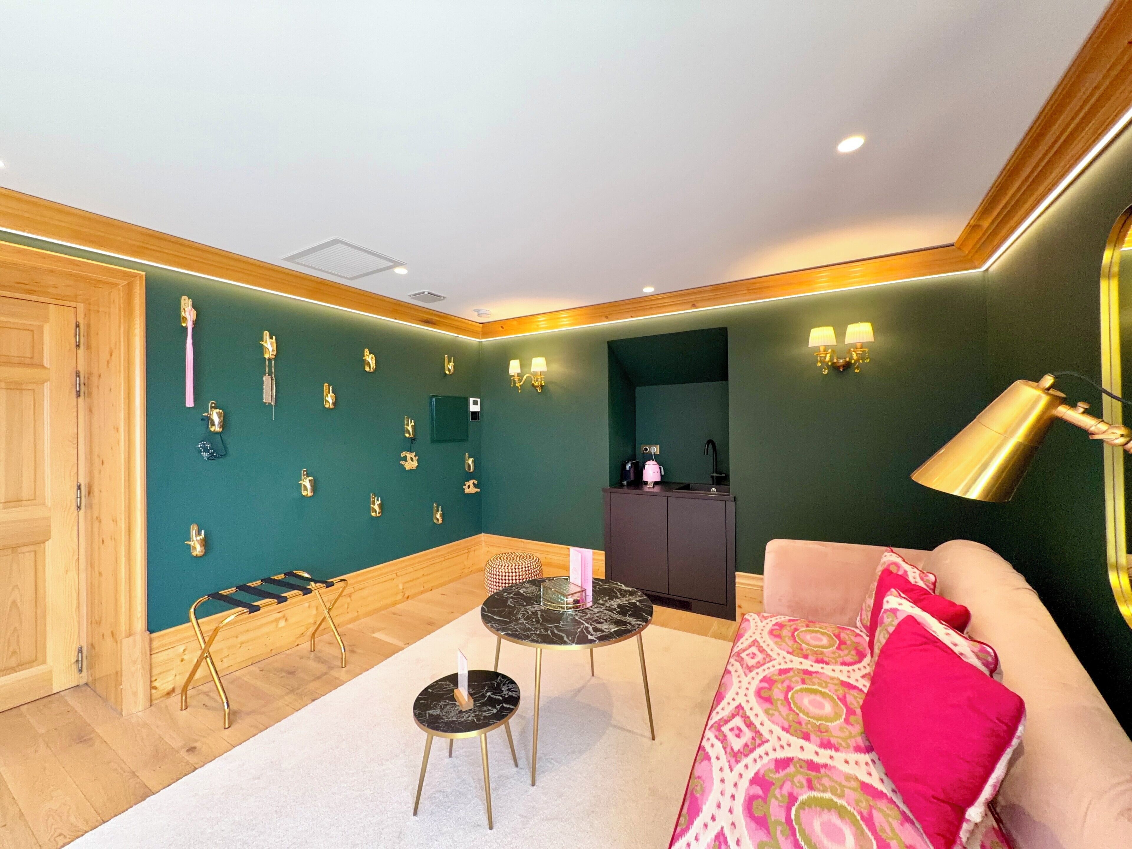 A room with a green wall, a wooden door, a black marble table, a pink sofa, and a gold lamp.