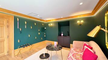 Een kamer met een groene wand, een houten deur, een zwart marmeren tafel, een roze bank en een gouden lamp.