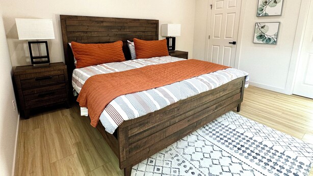 A bedroom with a wooden bed, two bedside tables with lamps, a patterned rug, and a door with artwork. - Boho luxury 2 master suites, huge yard (Alhambra)