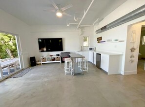 A modern kitchen with a large TV, white cabinetry, and a dining area with stools. - Casa Mar: private beach, pool & kayaks (Key Largo)