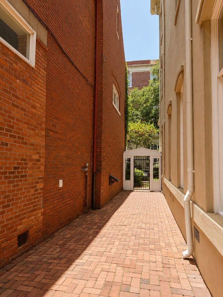 A narrow brick alleyway with a gated entrance, leading to a building with a white facade.