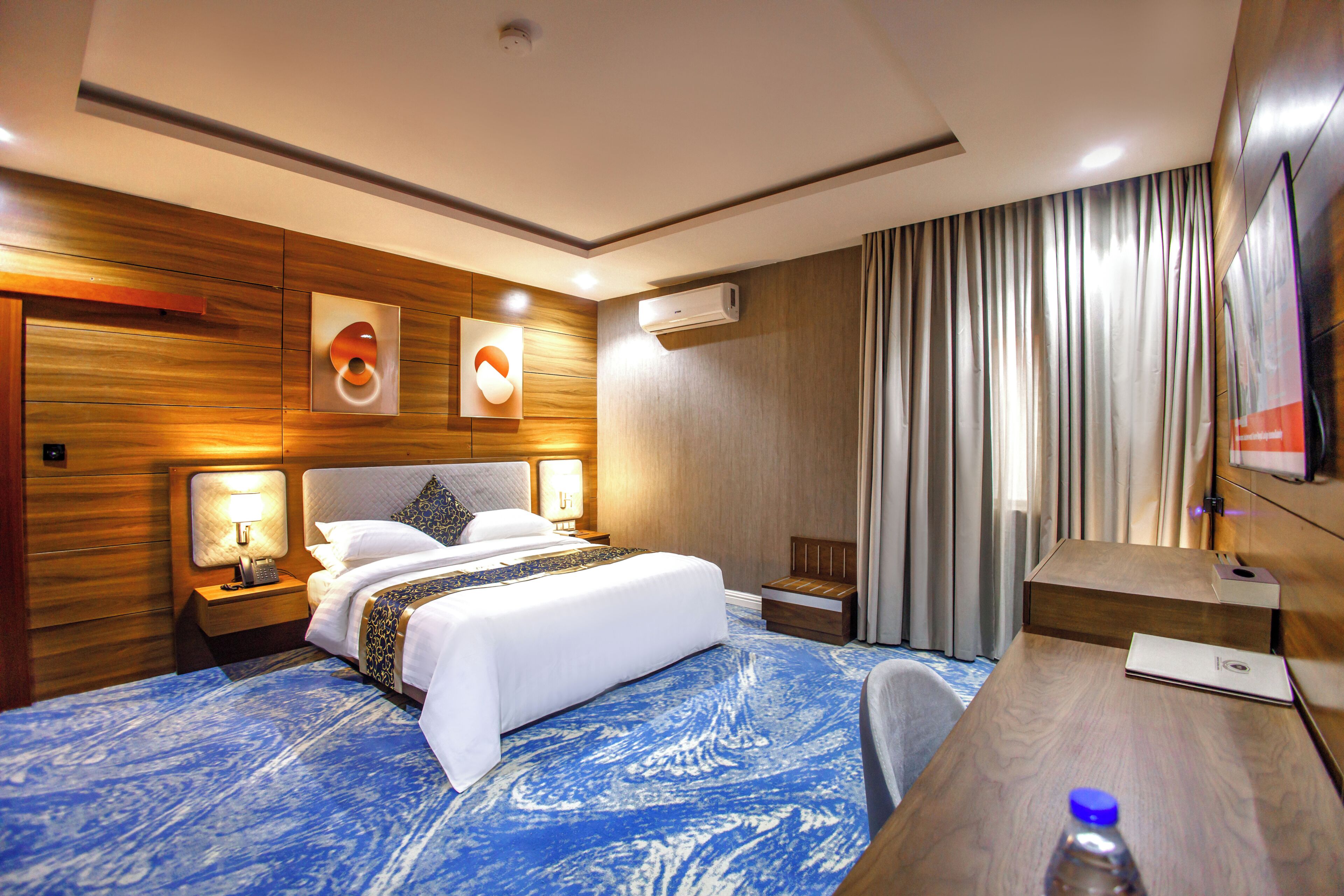 Ein Hotelzimmer mit Bett, Nachttischen, Schreibtisch, Sessel und Vorhängen.
