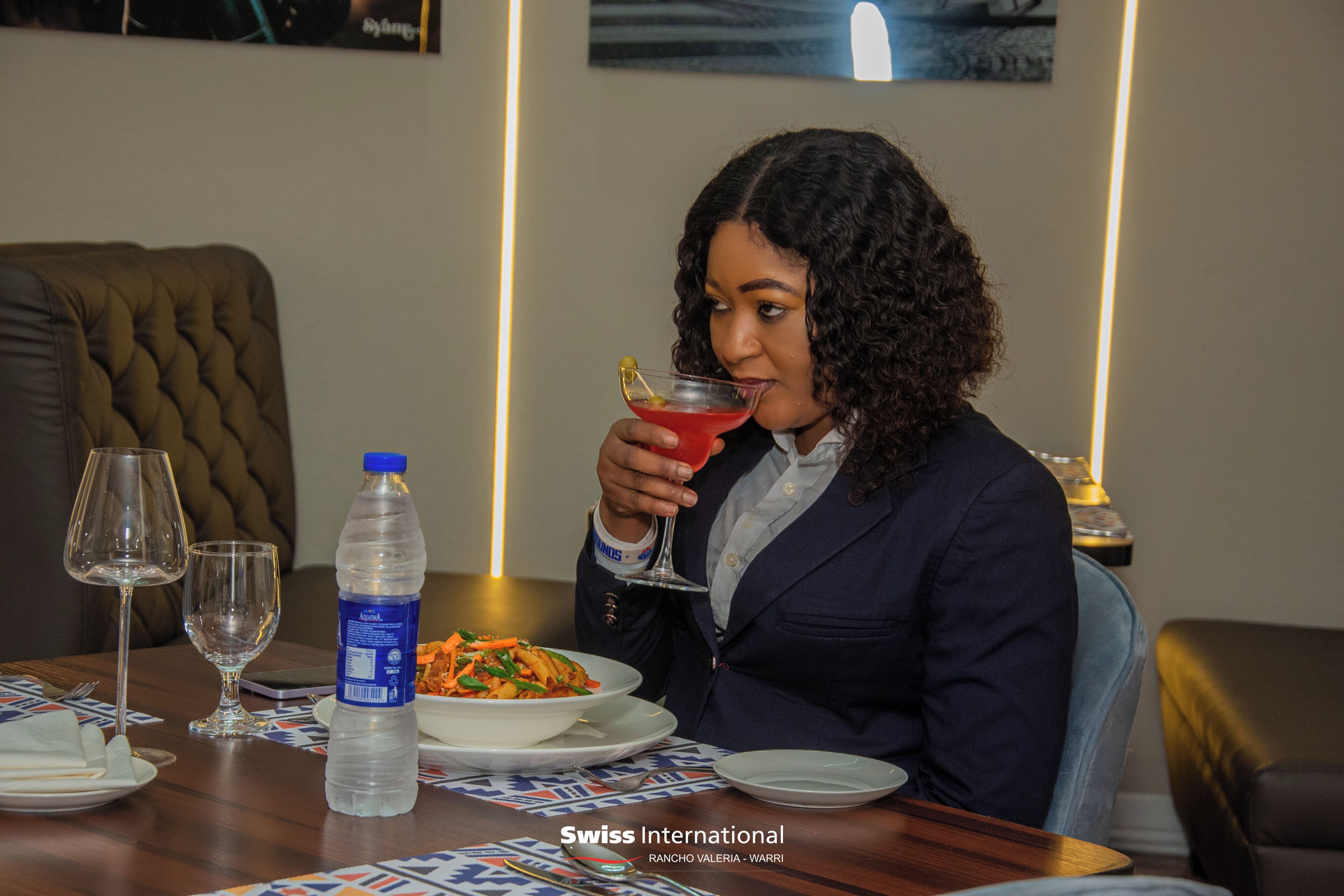 A dining table with a bottle of water, a glass of red drink, and a plate of food.
