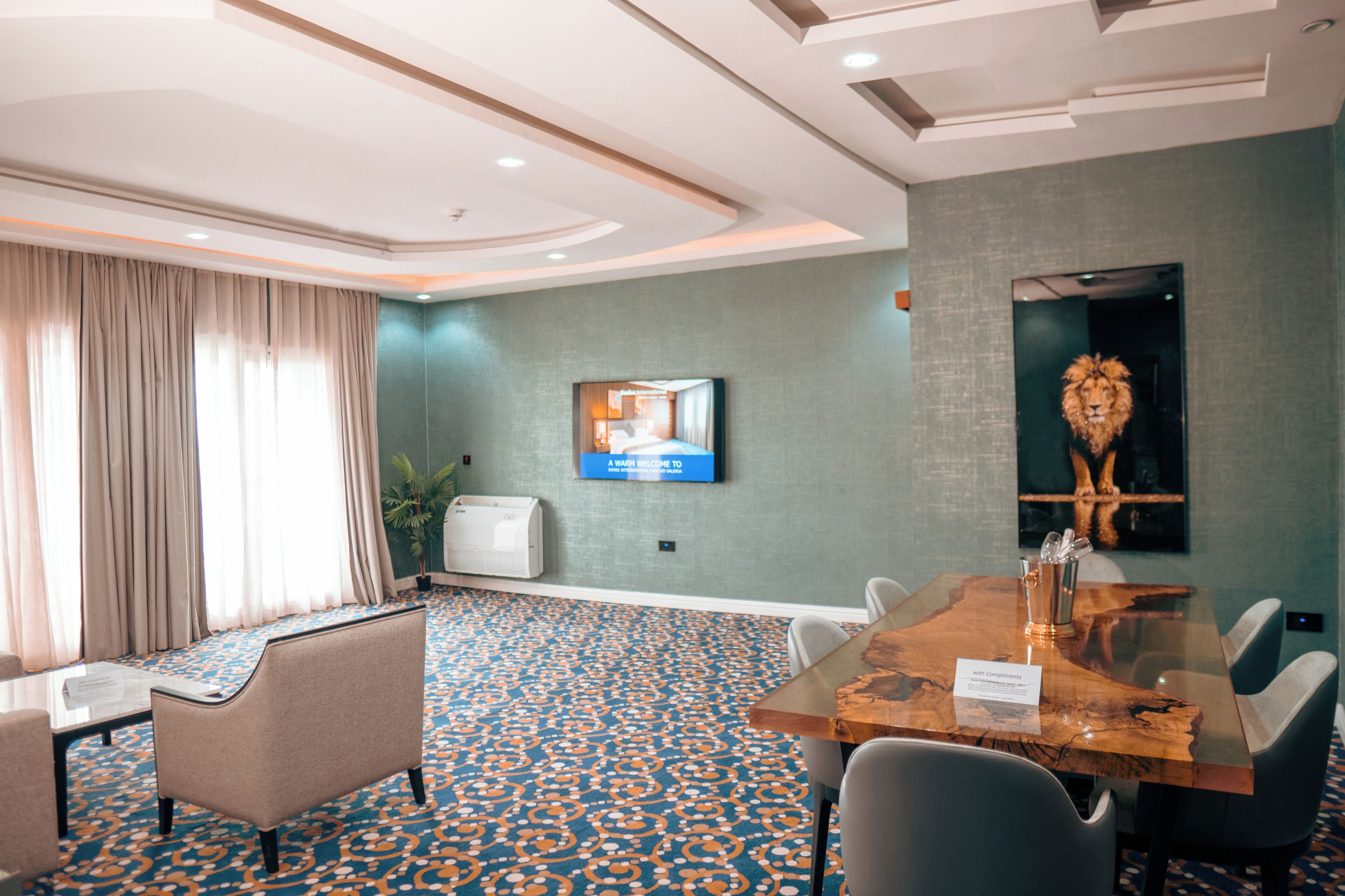 A conference room with a large wooden table, several chairs, a television mounted on the wall, and a lion head decoration.