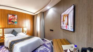 A hotel room with a bed, bedside lamps, a desk, and a television.