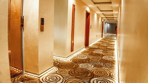 A hotel hallway with patterned carpet, wooden doors, and recessed lighting.