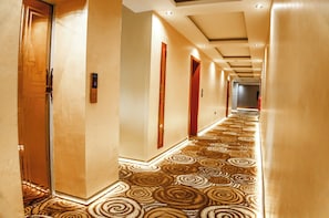 Un pasillo de hotel con alfombra estampada, puertas de madera e iluminación empotrada.