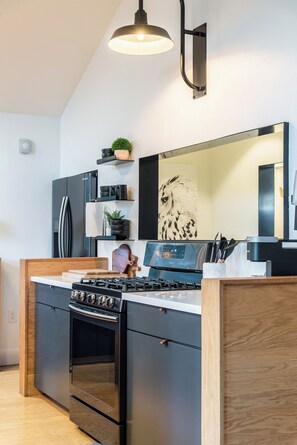 Een moderne keuken met zwarte kastjes, een roestvrijstalen koelkast, een gasfornuis en een houten eettafel.