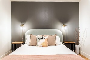 Een slaapkamer met een bed, kussens, nachtkastjes en wandlampen.