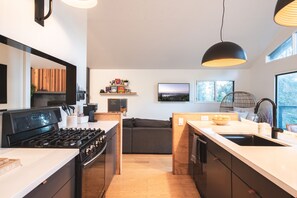 A modern kitchen with a stove, sink, and wooden cabinets. There is a dining area with a table and chairs, and a view of the outdoors through a window. - Amazing 5 bedroom house in peaceful Lake Arrowhead getaway (Lake Arrowhead)