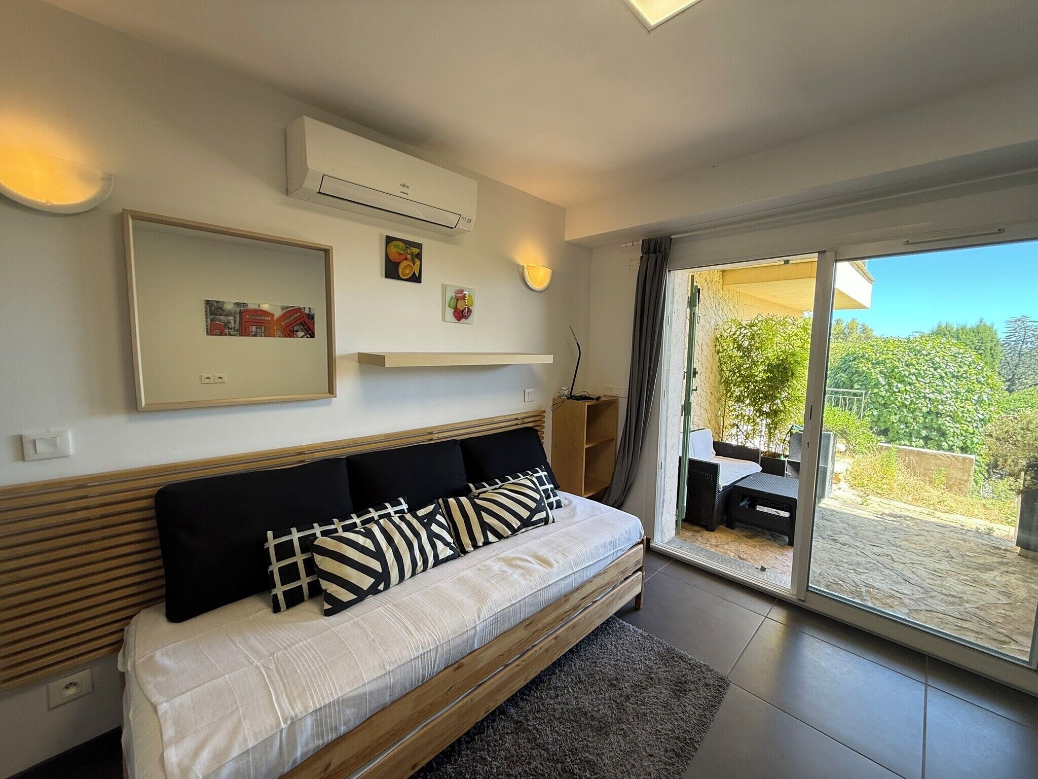 A bedroom with a bed, a mounted air conditioner, a framed picture, and a sliding glass door leading to an outdoor area.