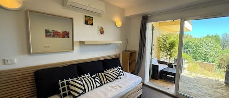 A bedroom with a bed, a mounted air conditioner, a framed picture, and a sliding glass door leading to an outdoor area.