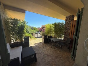 An outdoor patio area with a stone floor, a table with chairs, and various potted plants.