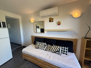 A modern bedroom with a bed, bedside lamps, a mirror, and a small kitchen area. - Studio climatisé avec terrasse au calme - La Garde (La Garde)