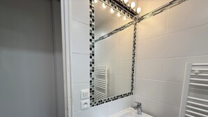 A bathroom with a white sink, a mirror with black mosaic borders, and a towel rack. - Studio moderne, climatisé, avec grande terrasse - La Garde (La Garde)