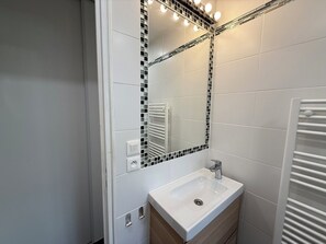 Un baño con lavamanos blanco, un espejo con bordes de mosaico negro y un perchero para toallas.