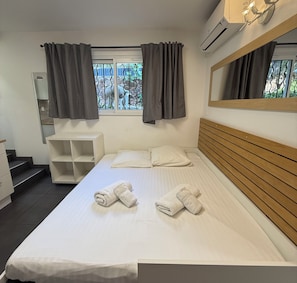 Een hotelkamer met een bed, nachtkastje, spiegel, raam met gordijnen en een airconditioning.