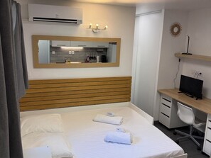 Habitación de hotel con una cama, un escritorio con computadora, un espejo y un equipo de aire acondicionado.
