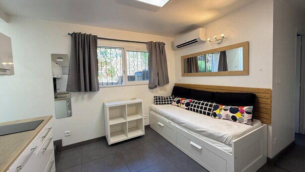 A bedroom with a bed, a bedside table, a wardrobe, a window with curtains, a mirror, and an air conditioning unit. - Studio moderne, climatisé, avec grande terrasse - La Garde (La Garde)