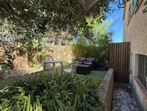 Un espacio patio con mobiliario exterior, un muro de piedra y diversas plantas.