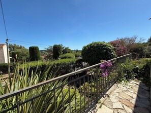 A garden with a stone pathway, metal railing, and various plants including a large bush and flowering plants. - Studio cosy dans villa, climatisé, terrasse - La Garde (La Garde)
