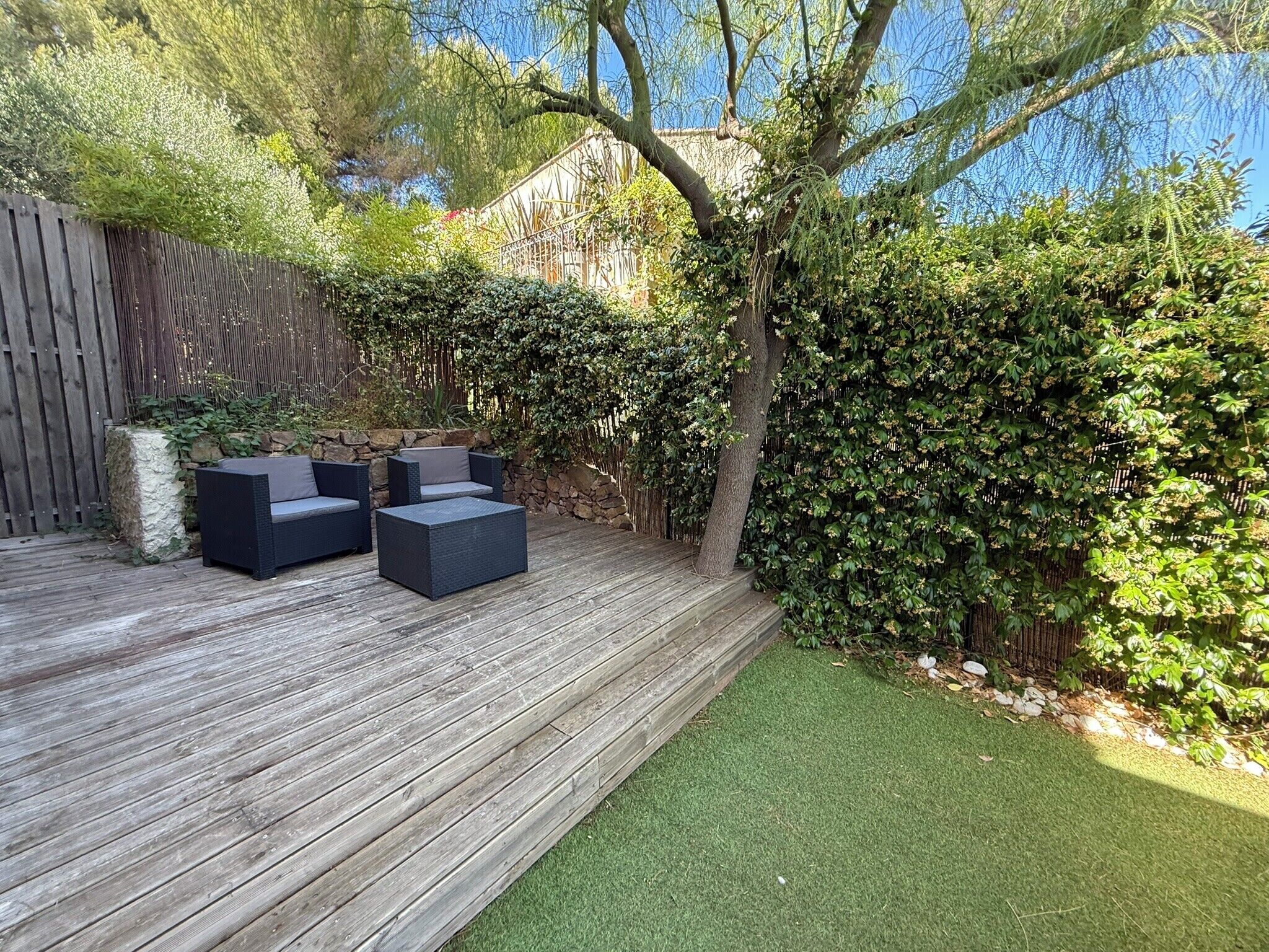 Une terrasse en bois avec des meubles d’extérieur, un mur en pierre et une haie.