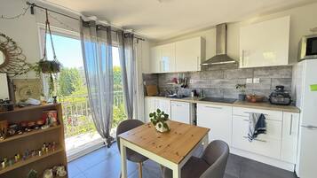 Een moderne keuken met witte kastjes, een houten tafel en uitzicht op groen.