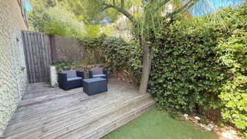 Une terrasse en bois avec des meubles d’extérieur, un mur en pierre et une haie dense.