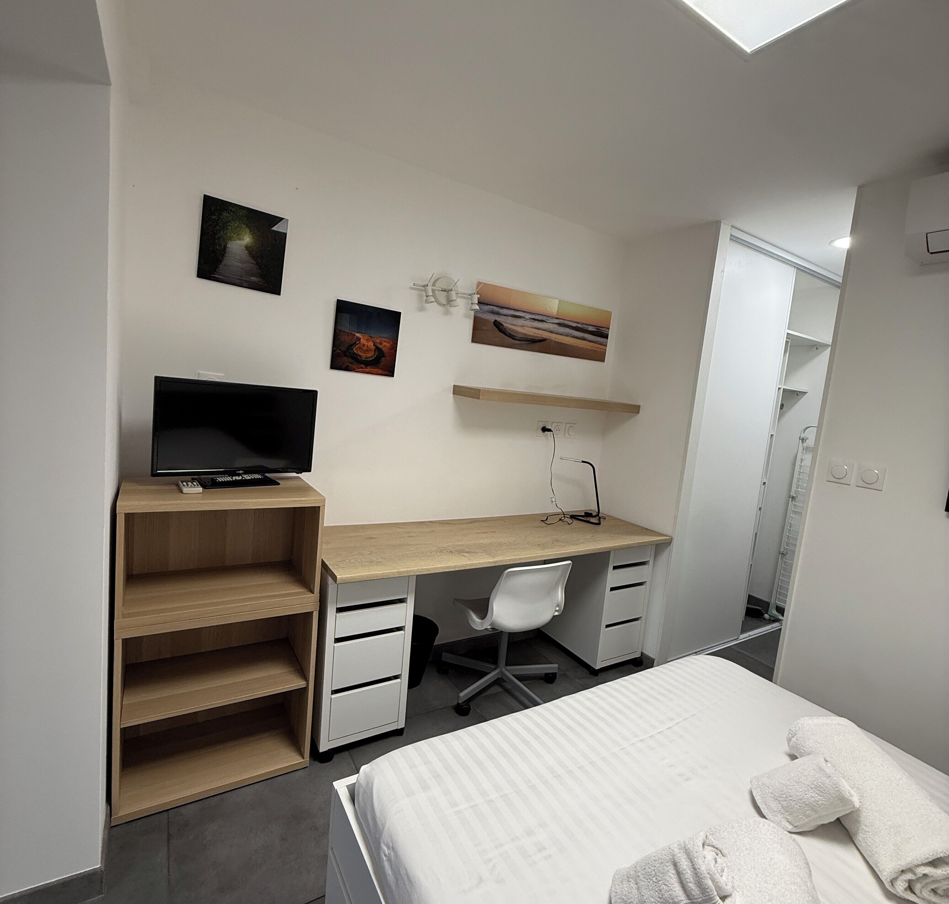 A bedroom with a bed, a desk, a chair, and a TV.