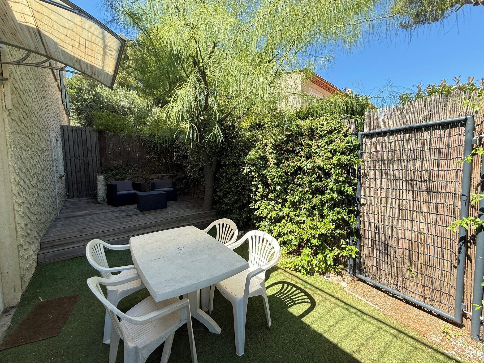 Une terrasse avec une table et des chaises, entourée d’une plateforme en bois et d’une clôture en bambou.