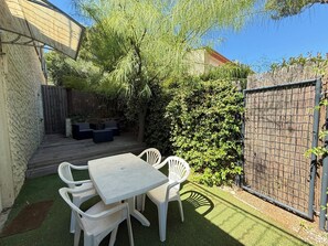 A patio with a table and chairs, surrounded by a wooden deck and a bamboo fence. - Studio cosy dans villa, climatisé, terrasse - La Garde (La Garde)
