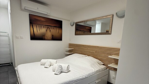 Ein modernes Schlafzimmer mit Bett, einem Gemälde, einem Spiegel und einer fest installierten Heizung.