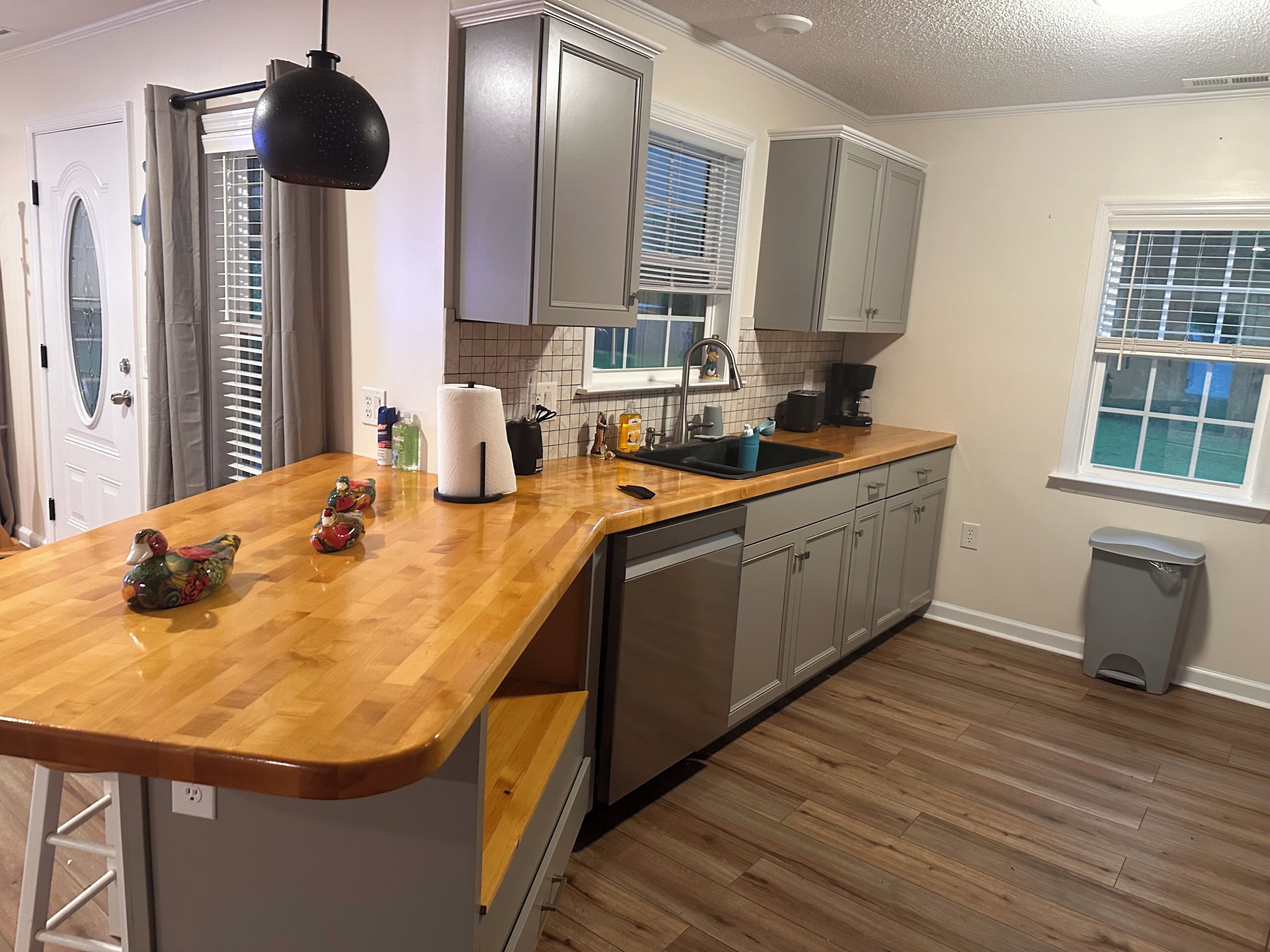 Una cocina con encimera de madera, armarios grises, lavavajillas y una ventana con persianas.
