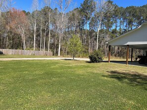 A grassy yard with a covered patio and a wooden fence.