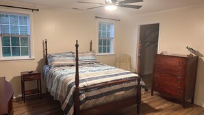 Een slaapkamer met een hemelbed, een houten dressoir, een stoel en een plafondventilator.