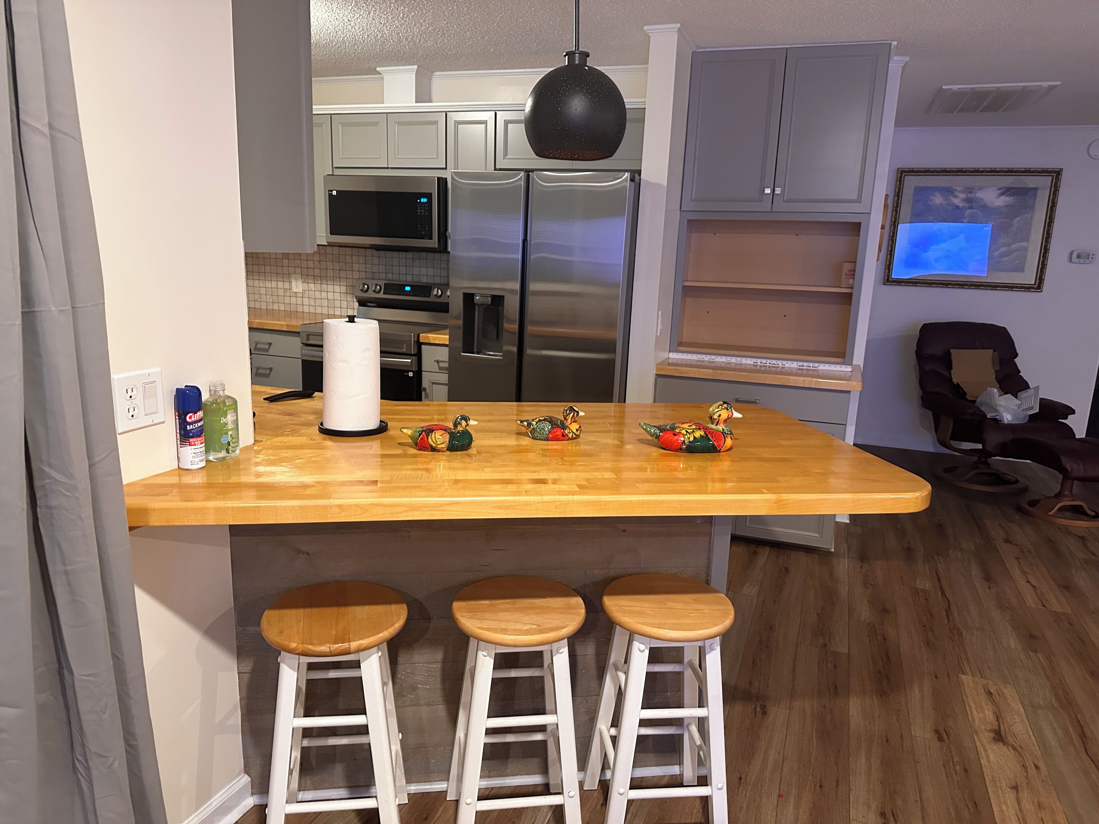A kitchen with a wooden island, bar stools, a microwave, a refrigerator, and a chair.