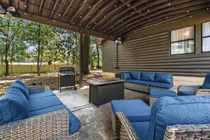 Eine Terrasse im Freien mit Korbmöbeln, einem Grill und einem überdachten Bereich mit Deckenventilator.