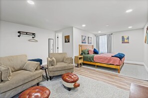 A bedroom with a bed, a sofa, a small table, and a hanging rack.