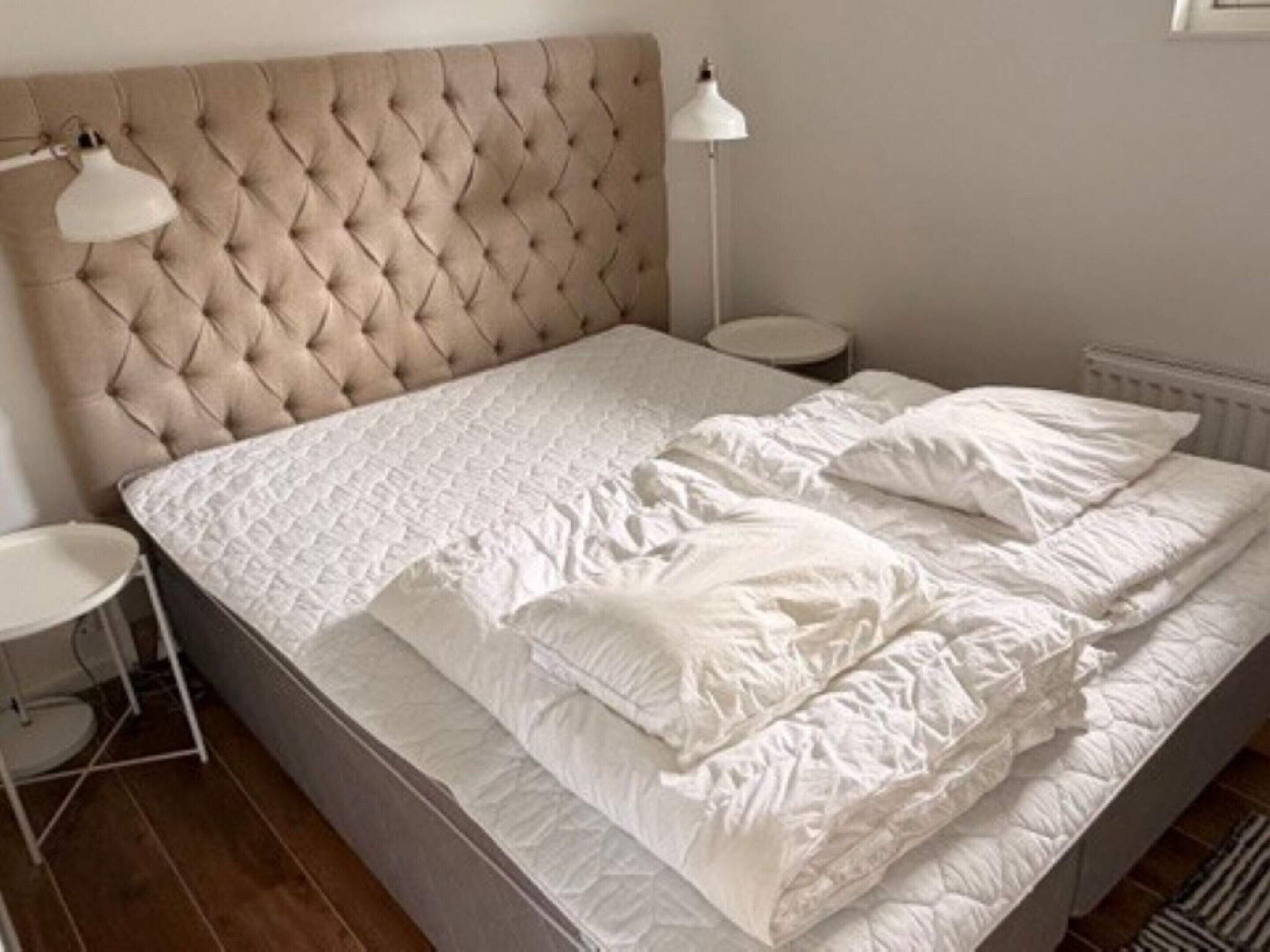 Una cama con cabecera capitonada, ropa de cama blanca y dos lámparas de noche.