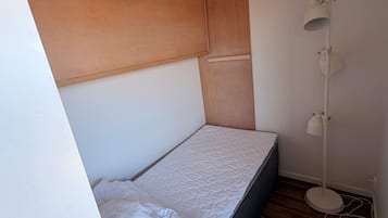 A small, single-bed room with a wooden headboard, a bedside lamp, and a wooden floor.