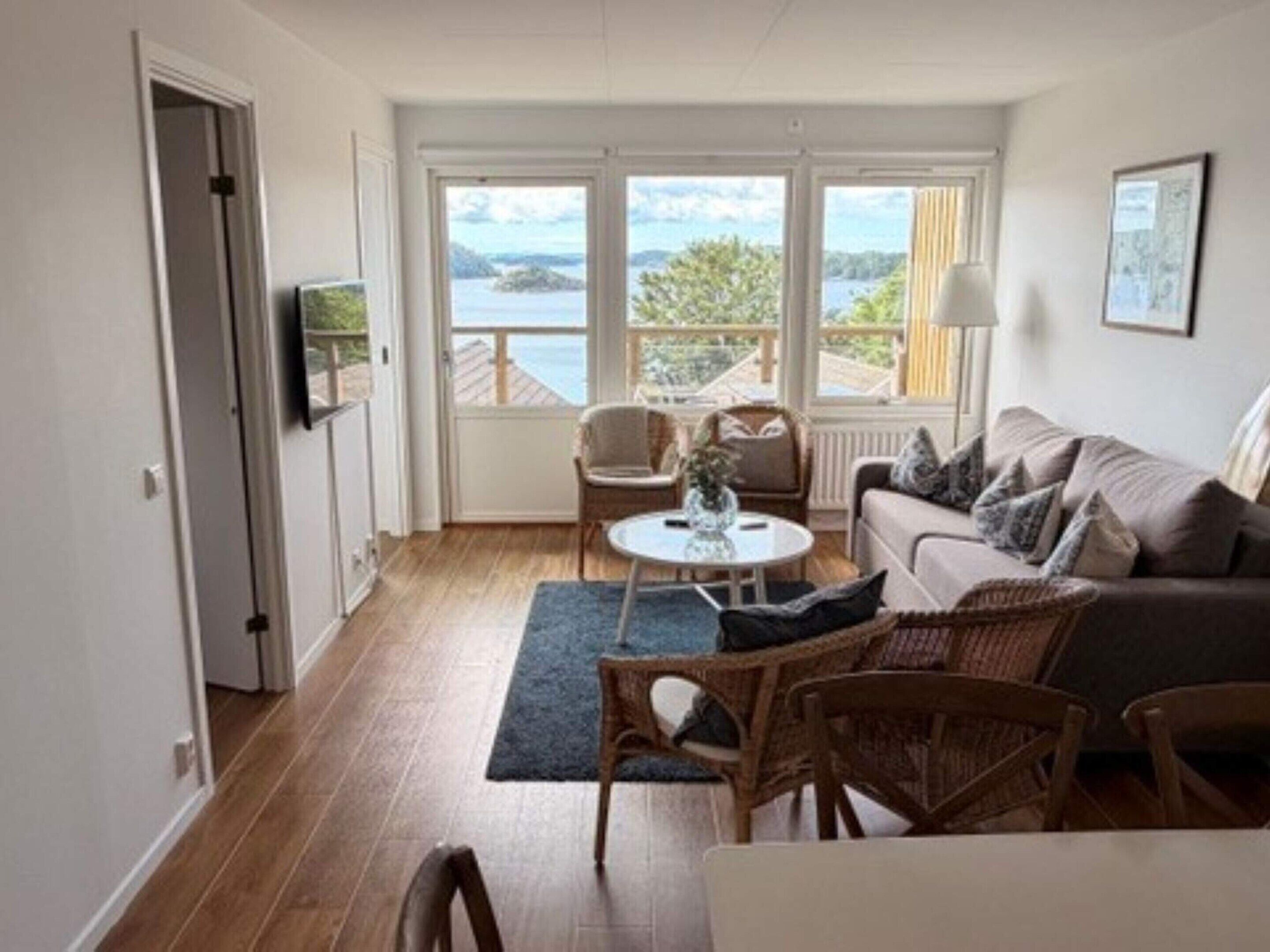 A room with a sofa, chairs, a table, and a view of the sea.