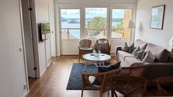A room with a sofa, chairs, a table, and a view of the sea.