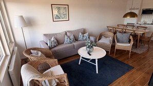 Uma sala de estar com um sofá, duas cadeiras de vime, uma mesa de centro e um espaço de jantar com cadeiras e mesa.