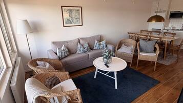 Una sala de estar con un sofá, dos sillas de mimbre, una mesa de centro y un comedor con sillas y una mesa.