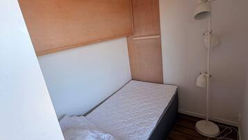 Una habitación pequeña con una cama individual, cabecera de madera, lámpara de noche y suelo de madera.