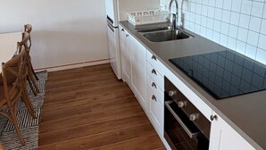 Uma cozinha compacta com armários brancos, bancada preta, pia de aço inoxidável e forno embutido.