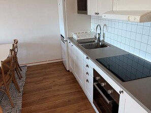 Eine kompakte Küche mit weißen Schränken, einer schwarzen Arbeitsplatte, einem Edelstahlspülbecken und einem eingebauten Backofen.