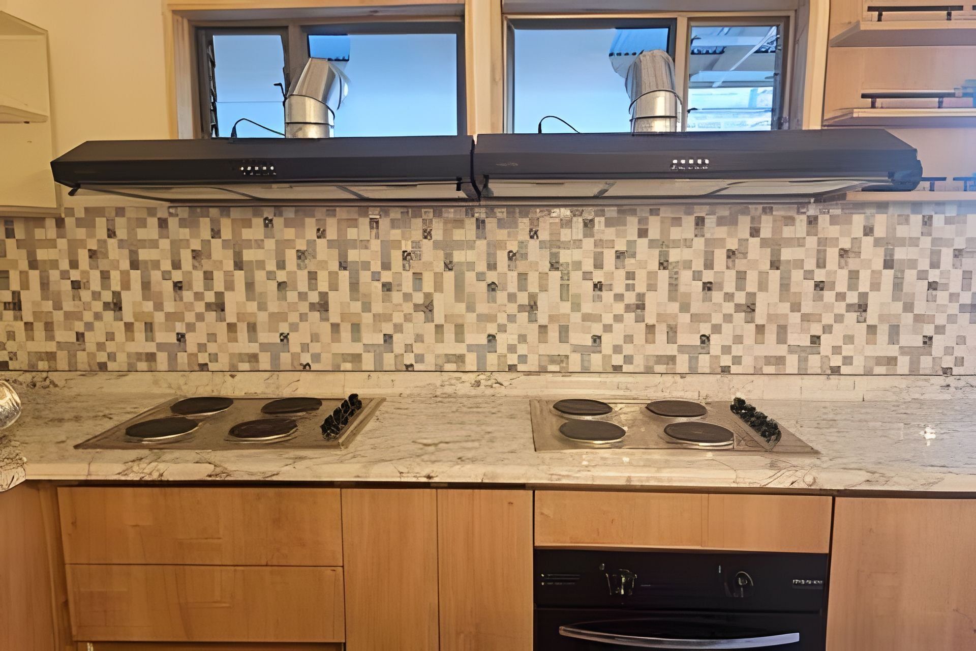 Une cuisine équipée de deux cuisinières à gaz, d’une hotte noire et d’un pare-feu en carreaux.