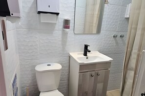 Ein Badezimmer mit Toilette, Waschbecken, Schrank, Spiegel und Handtuchspender.