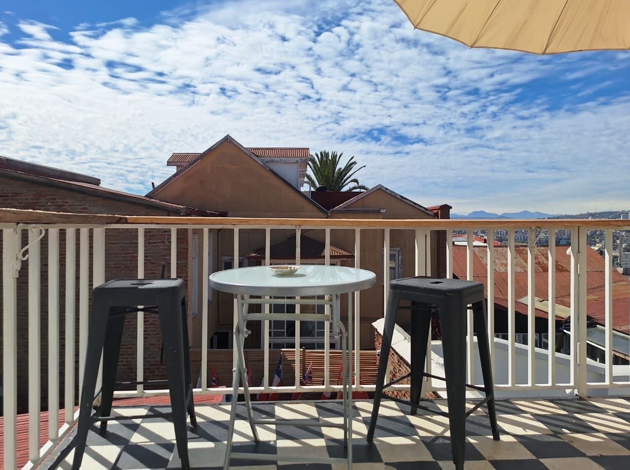A balcony with a checkered floor, two black stools, and a white table.